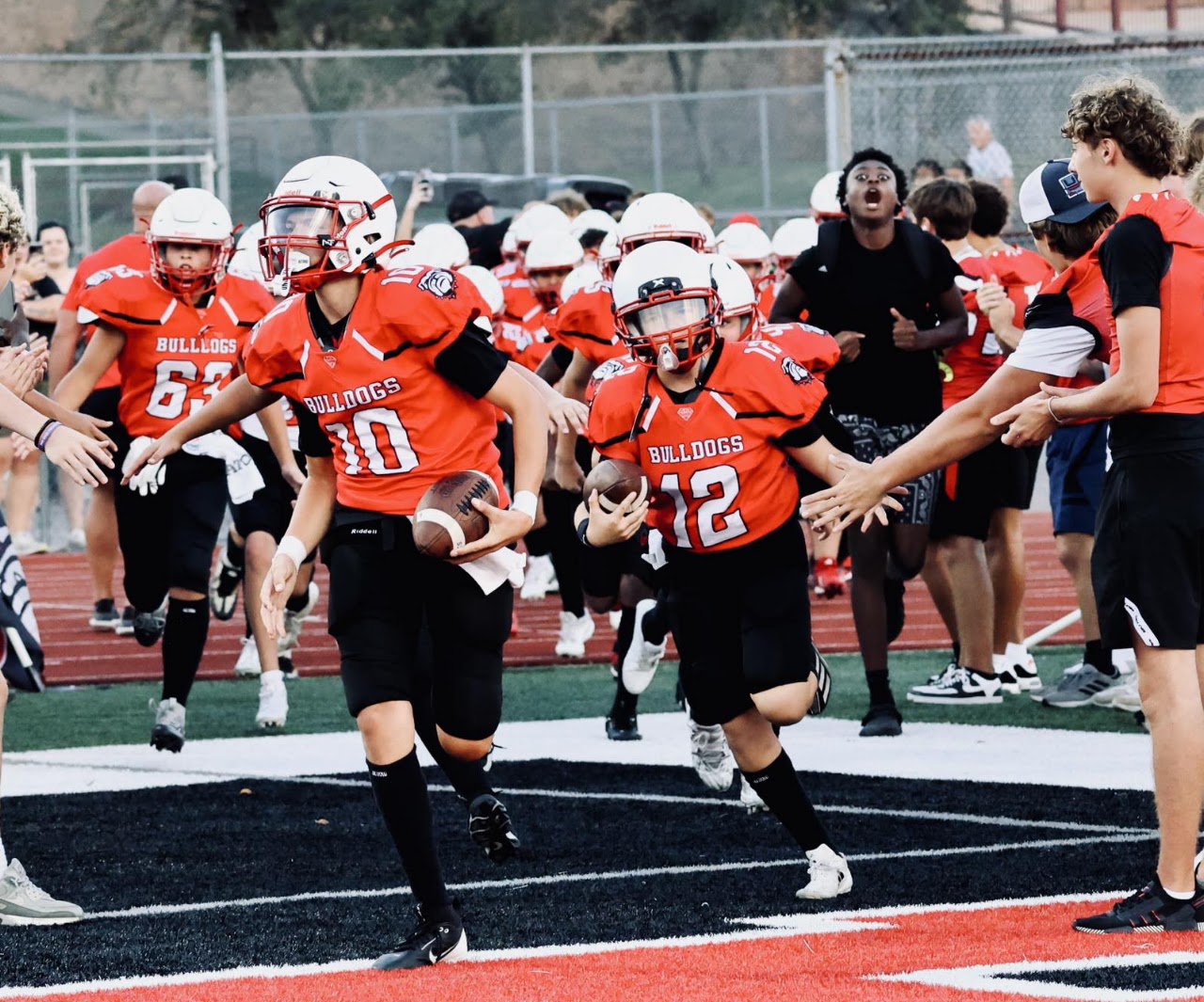 Junior Bulldogs football players running onto the field with teammates and supporters cheering